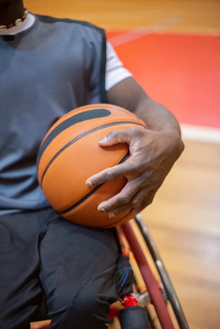 Close-up of a wheelchair basketball player holding a ball with determination on an indoor court.