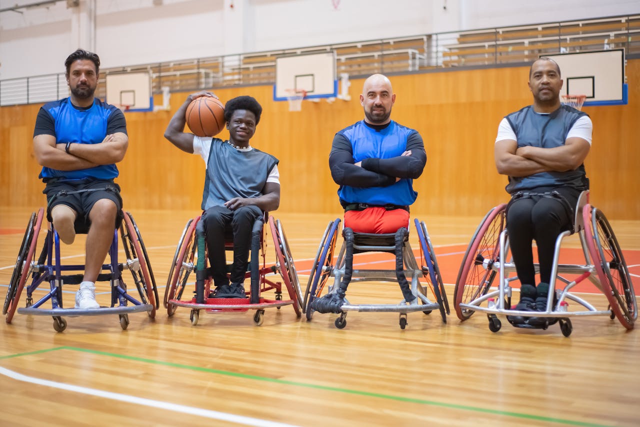 Four athletes in wheelchairs pose confidently on a basketball court, Portugal.